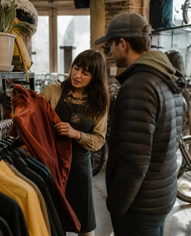 Shop staff member helping a customer choose a jacket inside an independent outdoor retail store
