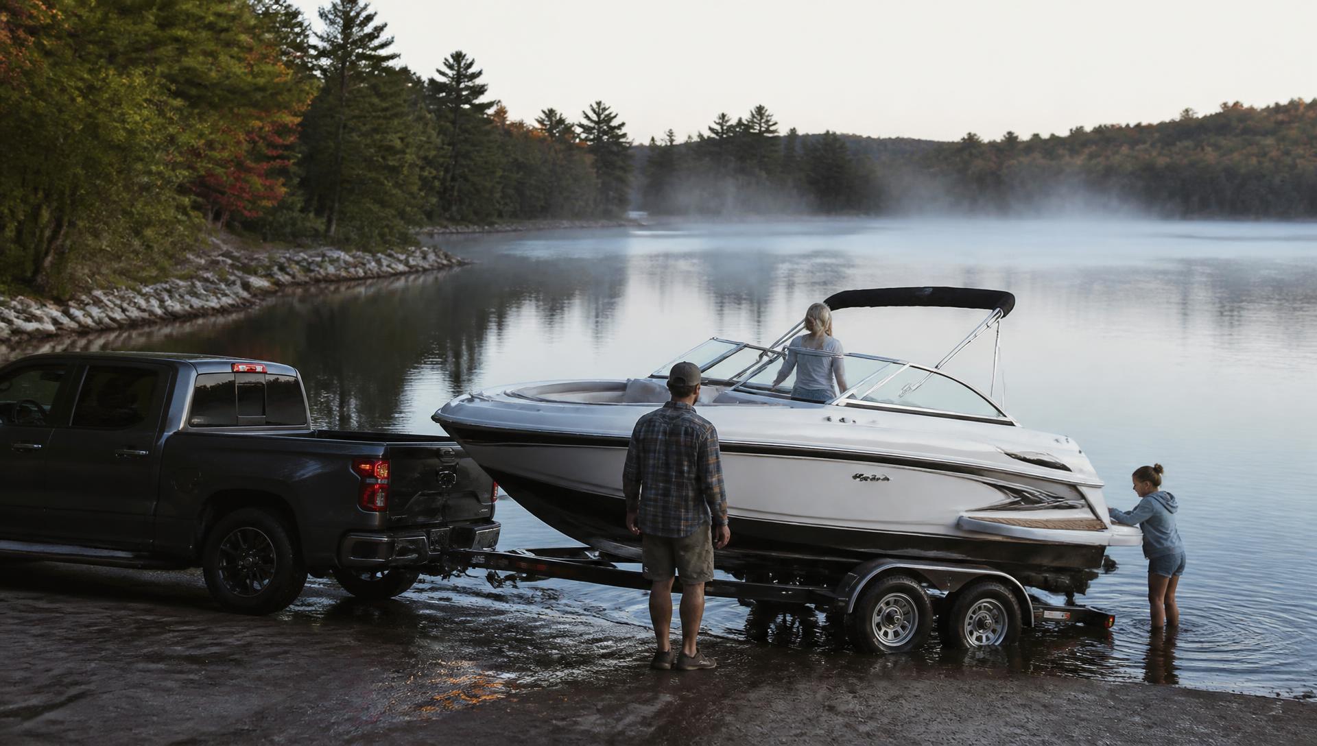 Family launching a newly delivered boat from a trailer at a quiet lake ramp in early morning light