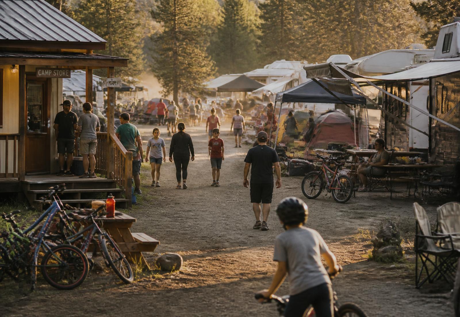 Busy campground at golden hour with occupied RV sites, bikes and guests walking toward the camp store