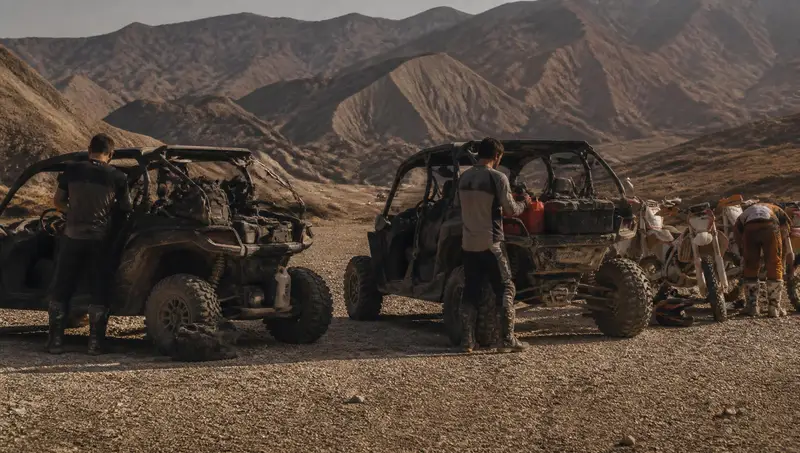 Riders unloading machines from a trailer at a gravel trailhead in early morning light