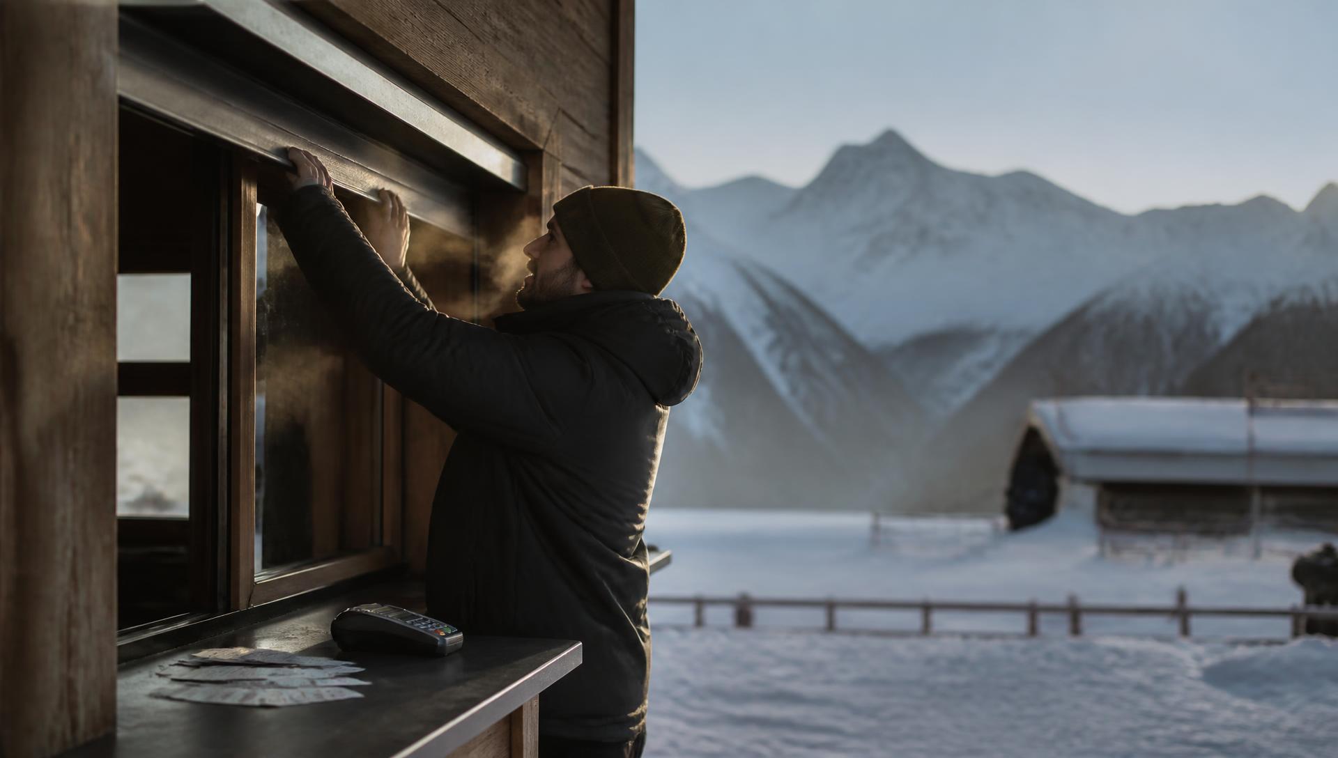 Resort employee opening the ticket window at a mountain base area before first chair, card terminal and printed lift tickets on the counter
