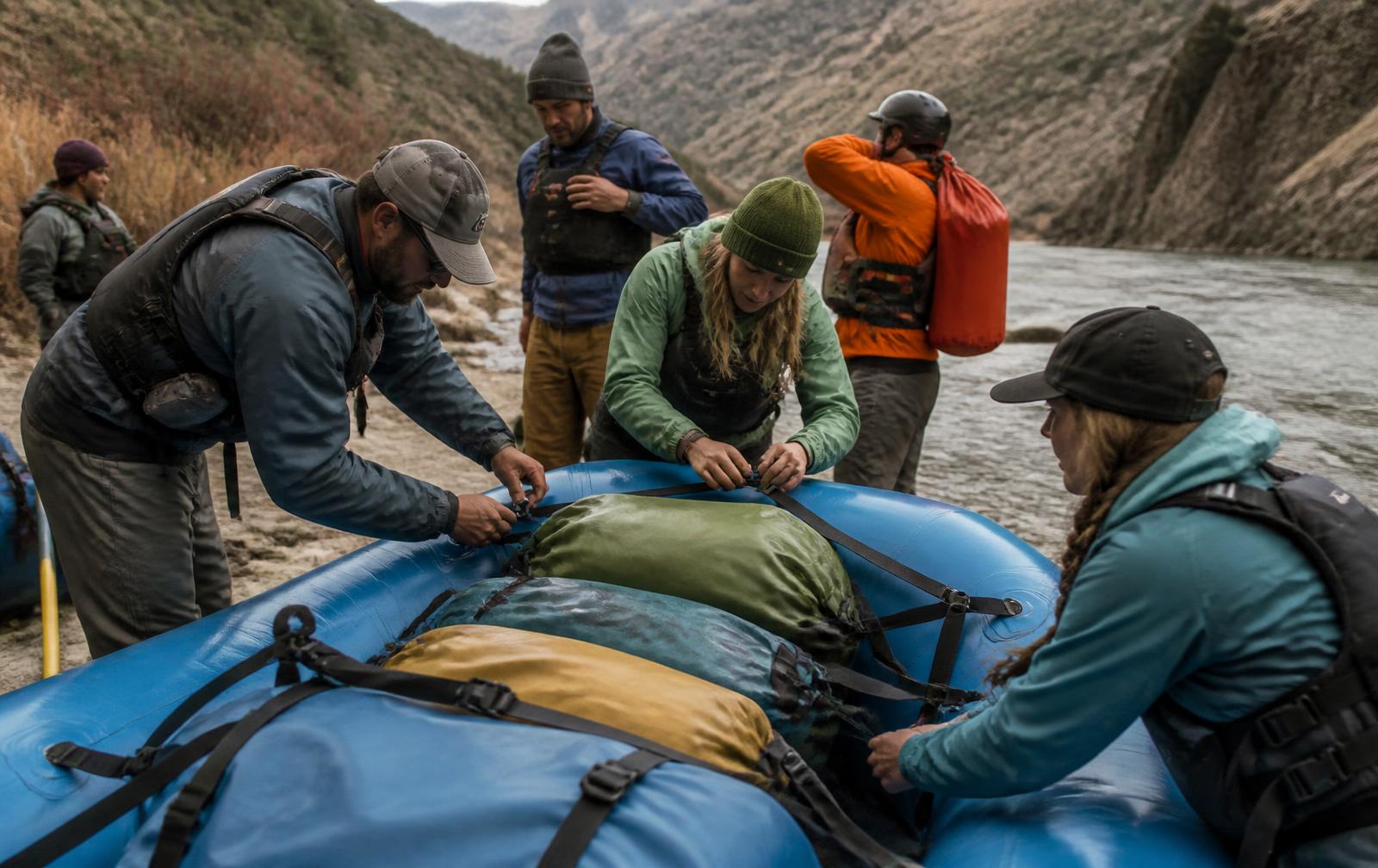 Guides and guests rigging and strapping dry bags onto a raft at a river put-in