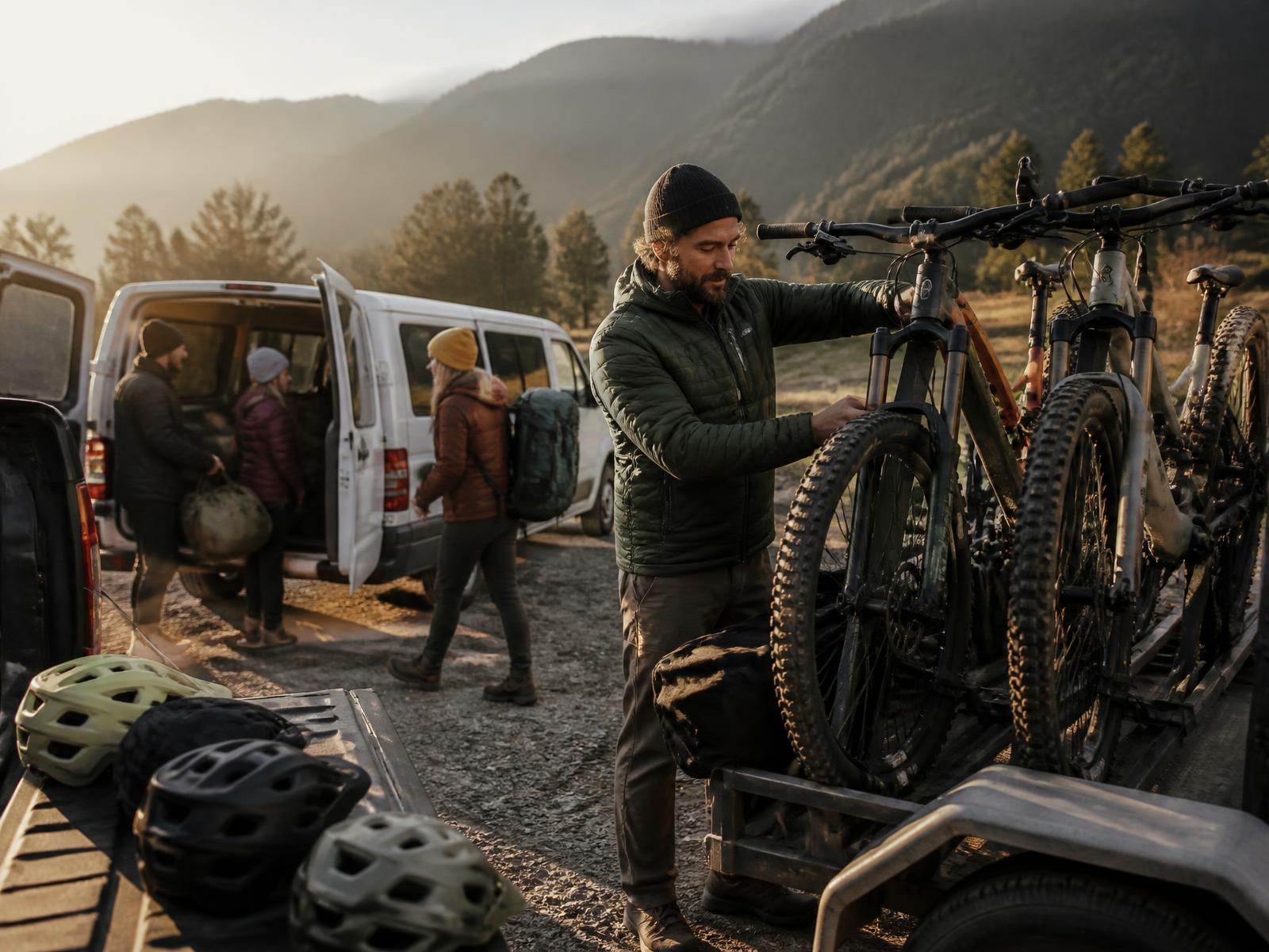 Tour guide unloading mountain bikes from a trailer while guests load duffels into a van at dawn