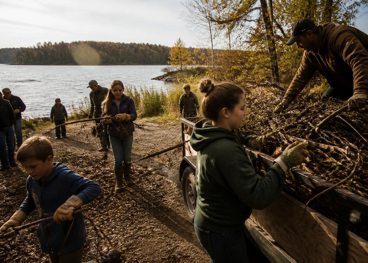Neighbours and families clearing brush onto a trailer during a lakeshore work day
