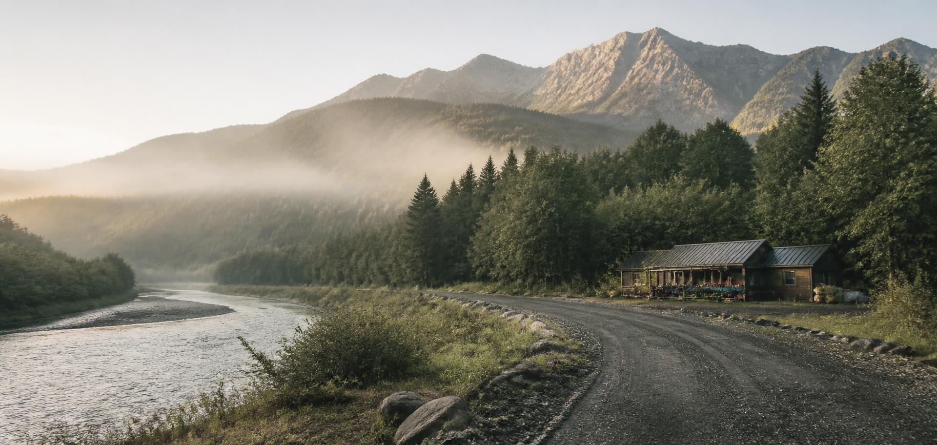 Mist over a river valley at sunrise with a small outfitter building at the forest edge