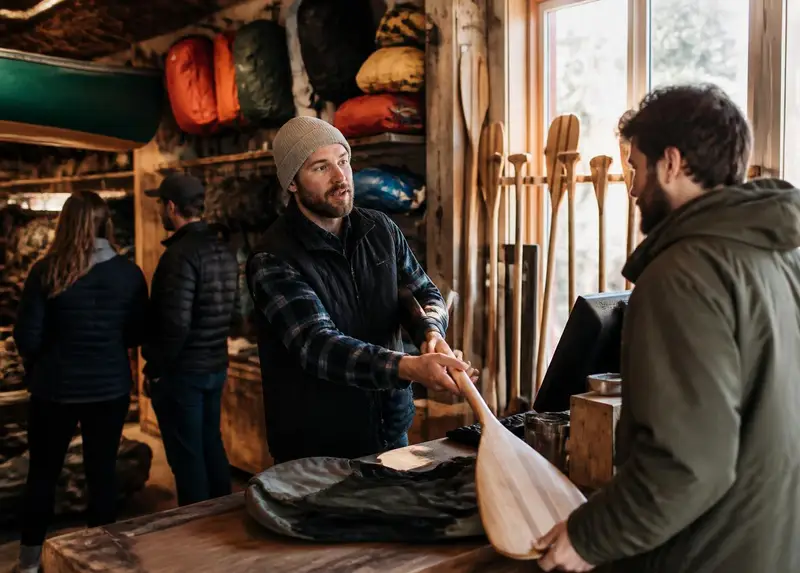 Staff member handing a paddle across the counter to a customer inside an independent outdoor gear shop