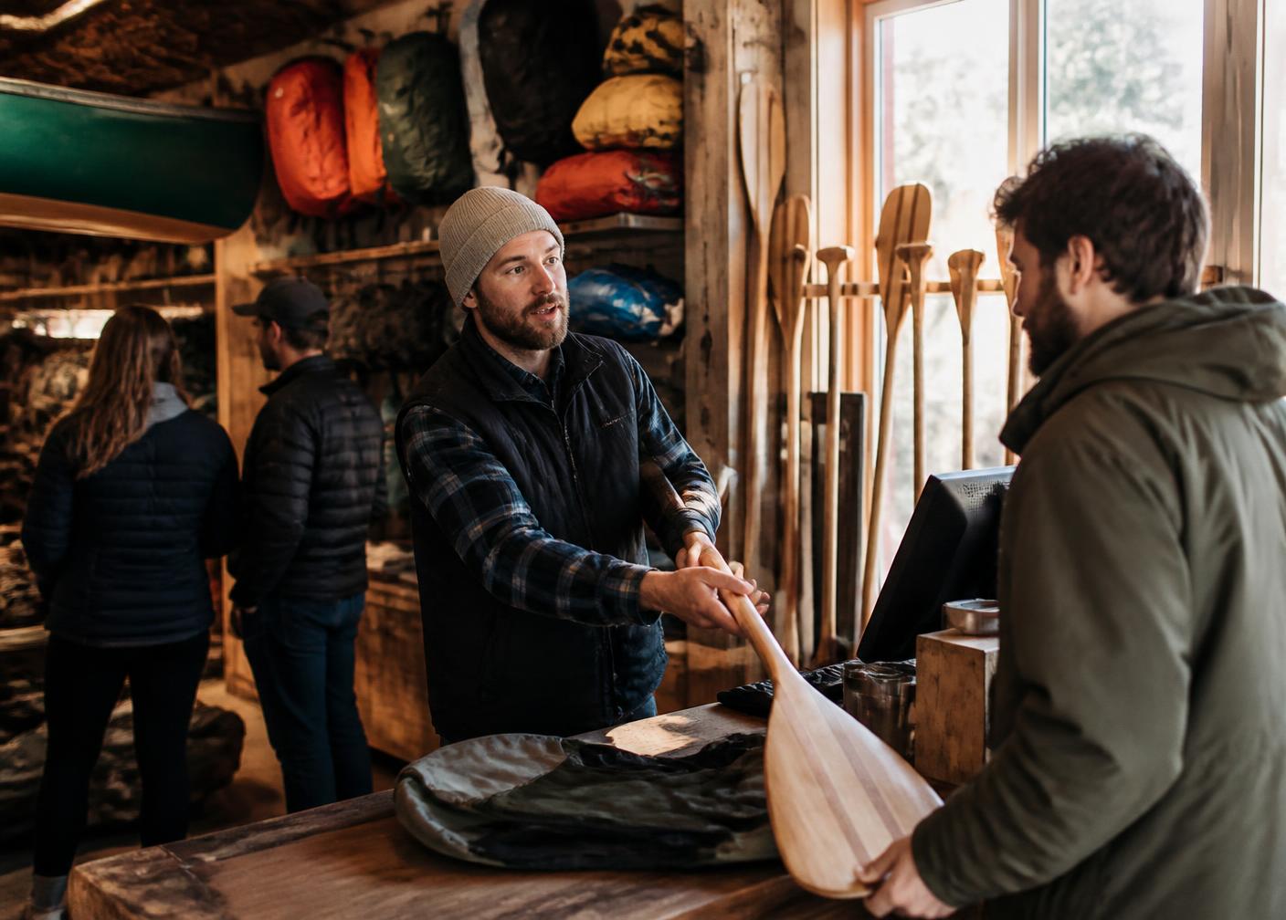Staff member handing a paddle across the counter to a customer inside an independent outdoor gear shop